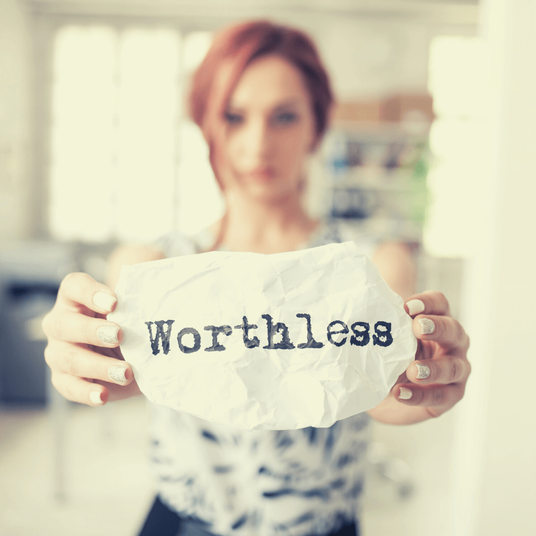 Eine Frau hält einen Zettel auf dem das Wort "wertlos" auf englisch steht.