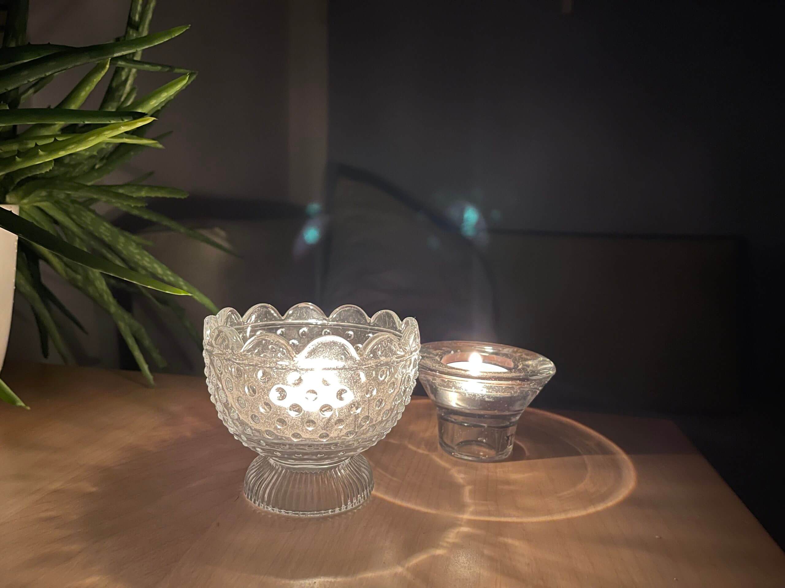 2 Teelichter stehen auf einem Tisch neben einer Pflanze im Dunklen