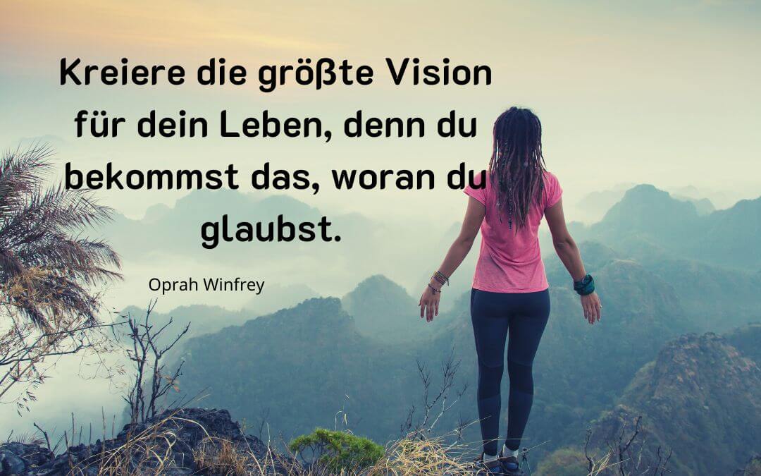 Frau steht oben auf einem Berg mit dem Zitat von Oprah Winfrey Kreiere die größte Vision für dein Leben denn du bekommst das woran du glaubst