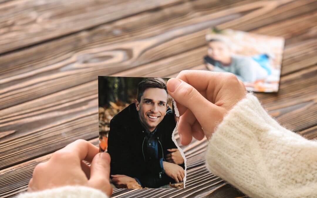Eine Frau sitzte an einem Tisch mit einem durchgerissenen Foto eines Mannes in der Hand und denkt über ihre Gefühle nach Trennung nach