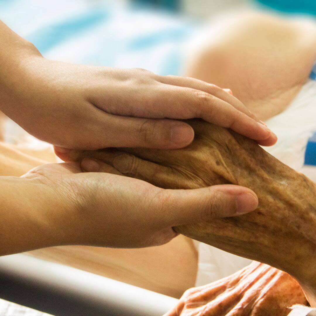 Im Krankenhaus hält jemand die Hand einer alten Frau