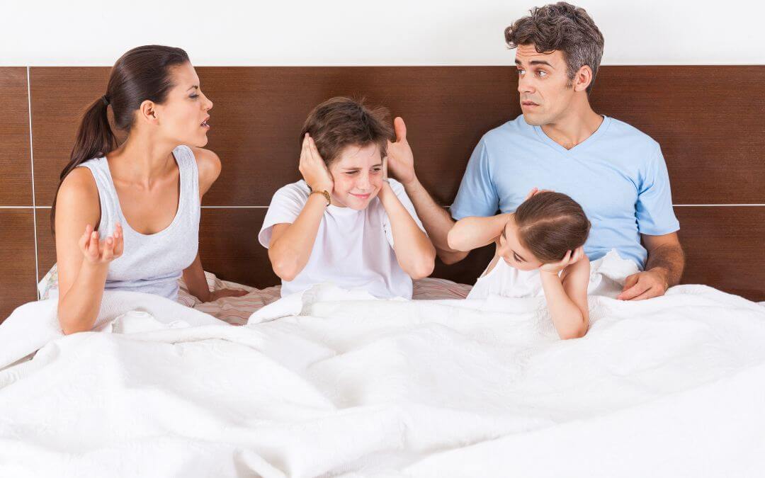 Mann und Frau streiten im Bett, in dem auch 2 Kinder sind